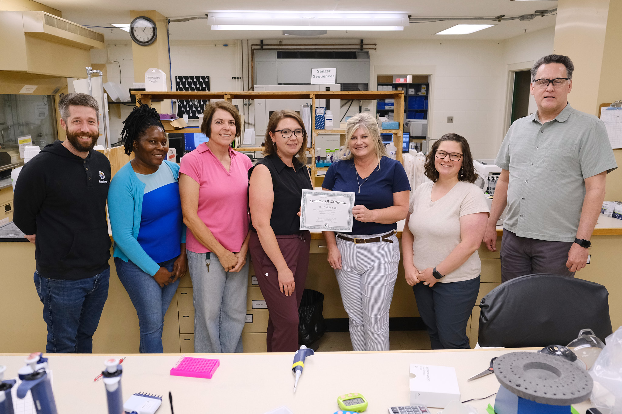 The Genomics Core staff standing in the wet lab with the safety certificate that was awarded.