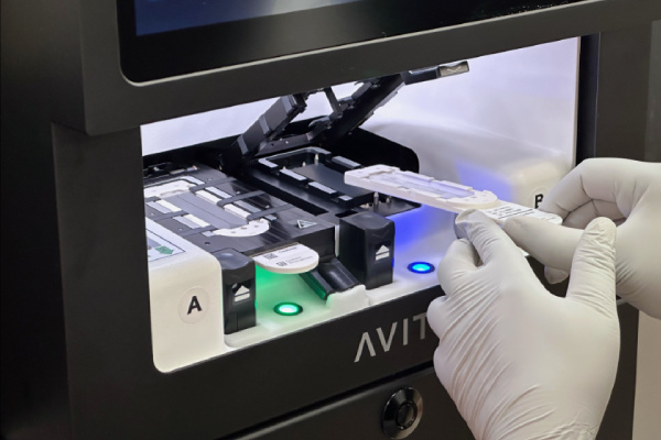 scientist wearing gloves placing test slide into a black and white machine for analysis